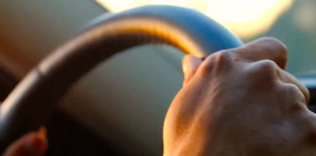 En person som kör bil där man bara ser en hand.