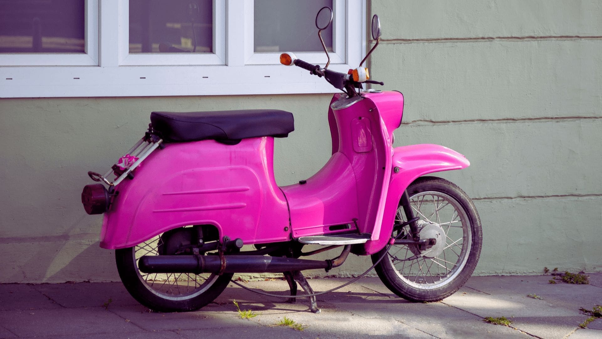 En rosa moped med ett hus i bakgrunden