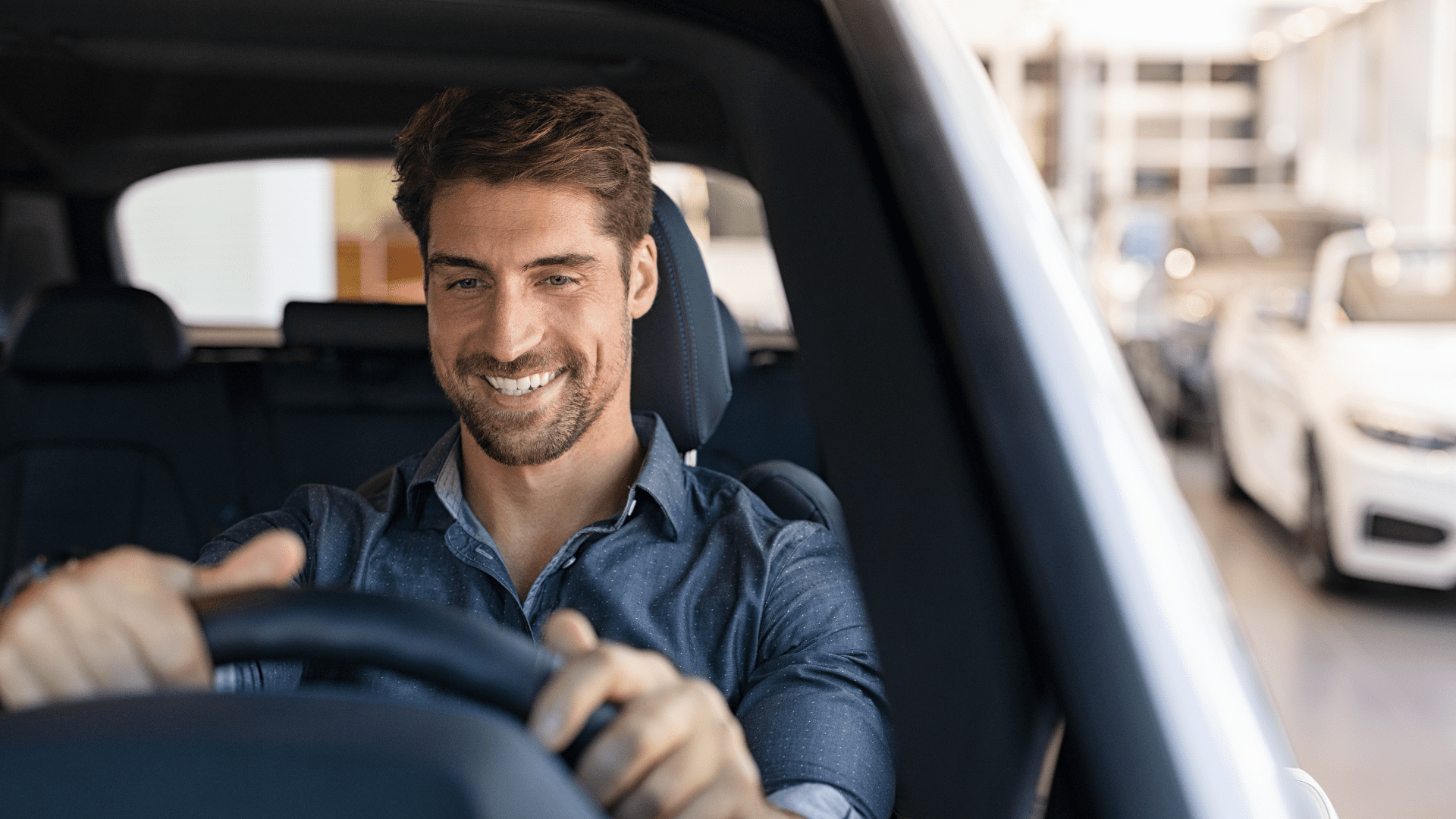 En vit mörkhårig man med trimmat skägg. Han sitter och kör i bilen och ler.